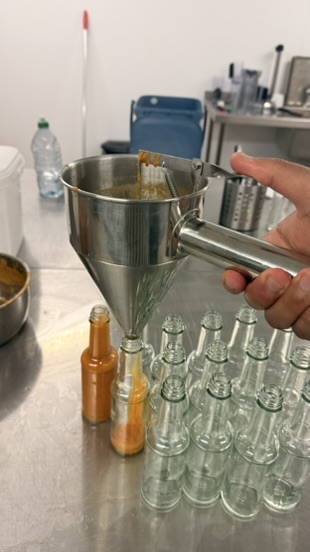 Hot sauce being poured through a metal funnel into glass bottles